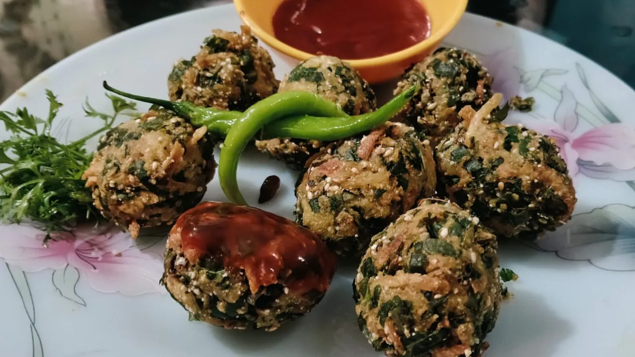 Golden crispy palak aloo khasta pakoda served on a white plate with fresh coriander leaves, green chillies, and tomato ketchup.