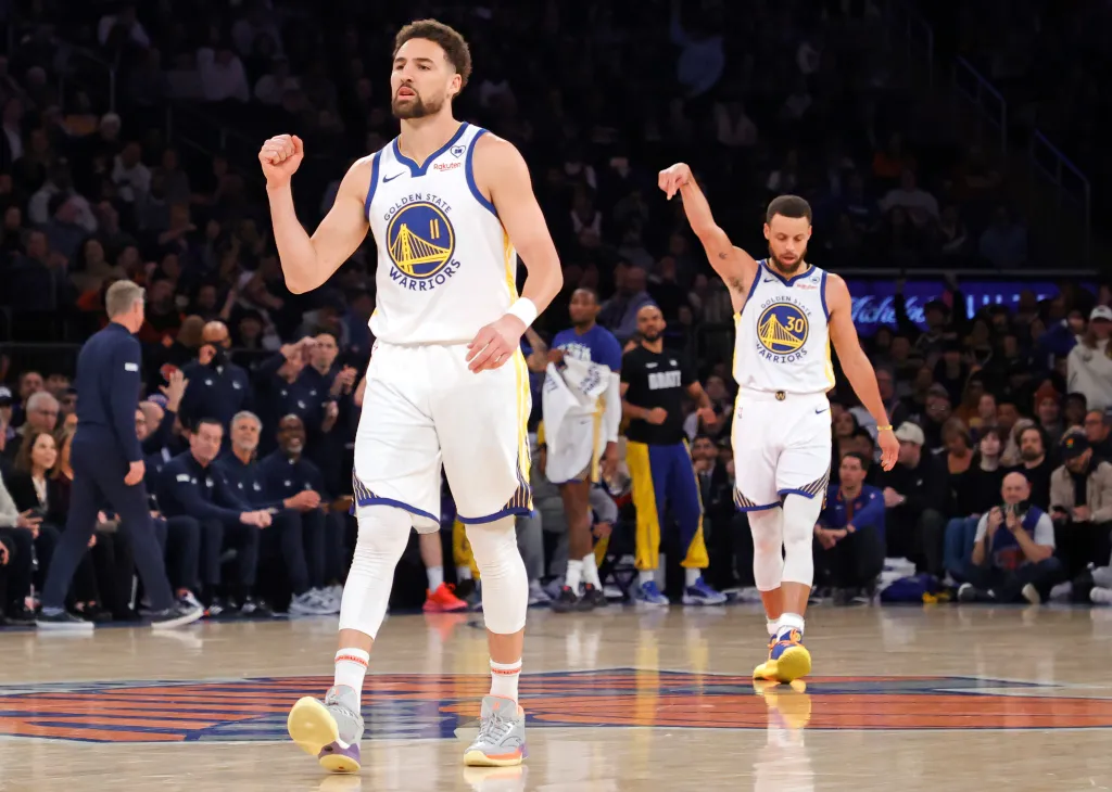 Klay Thompson and Stephen Curry in Golden State Warriors jerseys on a basketball court.