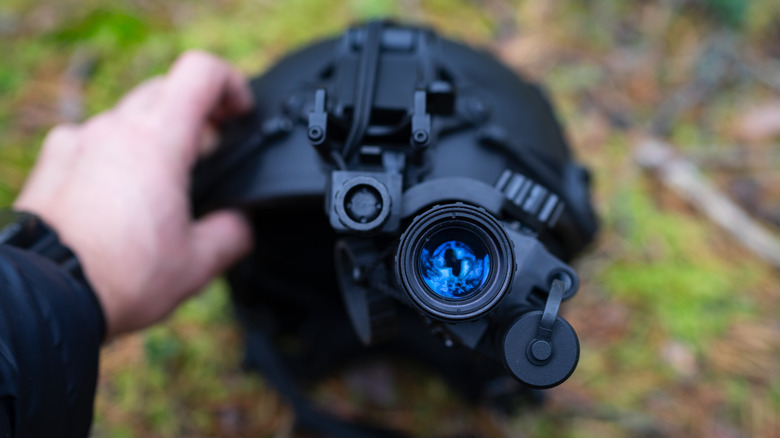 A person holding a helmet with a night vision viewer attached.