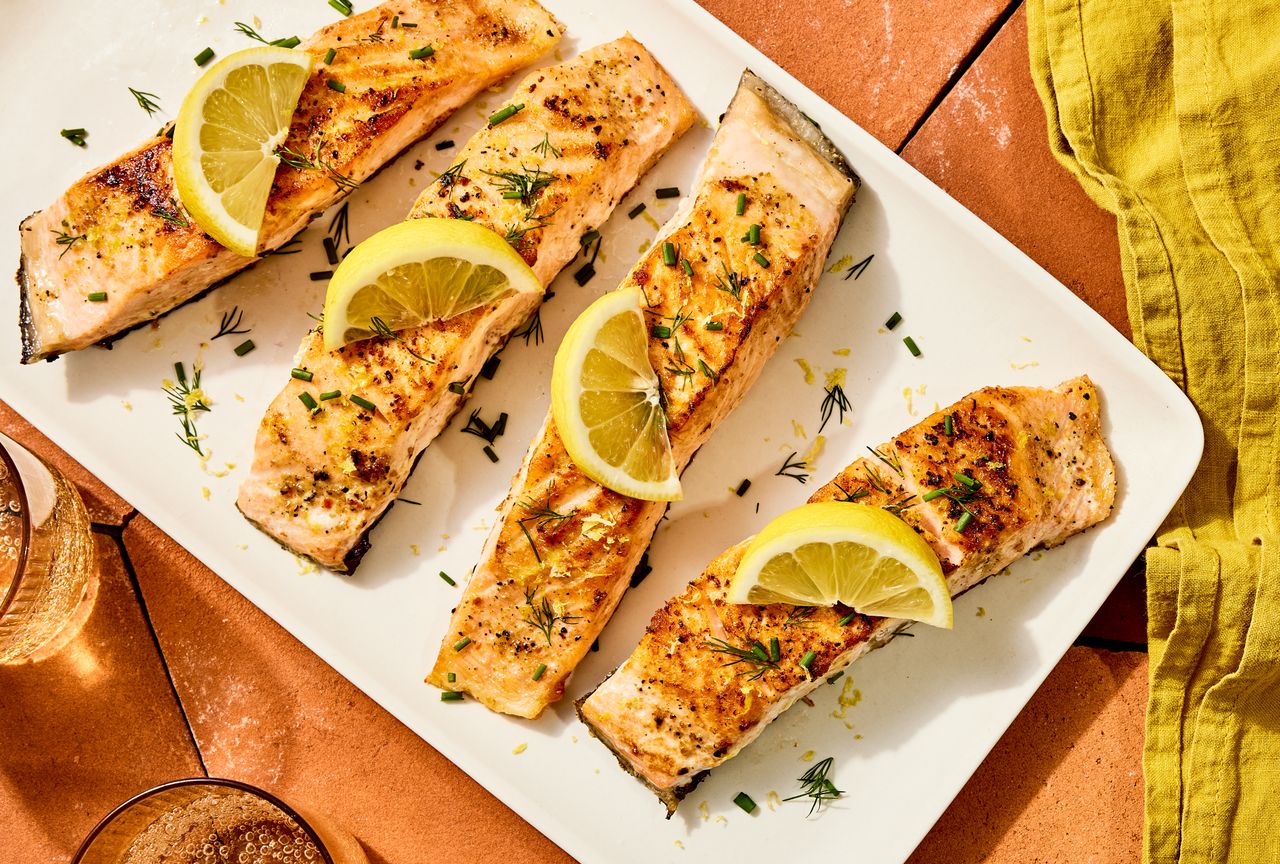 Four fillets of lemony-garlic pan-seared salmon on a white serving plate, topped wit lemon slices Credit: Photographer: Morgan Hunt Glaze, Food Stylist: Ruth Blackburn, Prop Stylist: Christine Keely