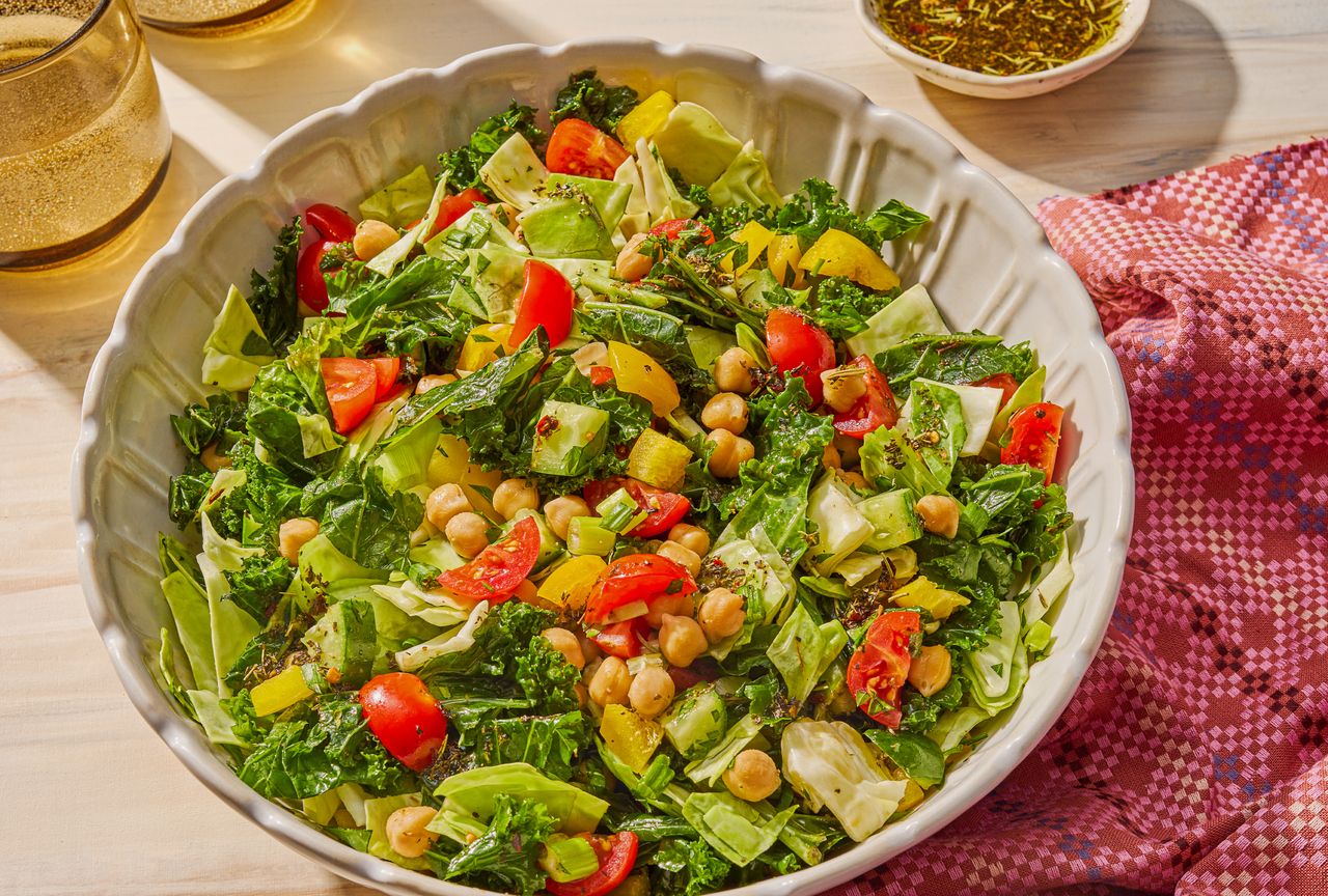Chopped salad in a white bowl featuring lettuce tomatoes chickpeas and a vinaigrette set on a lightcolored surface with a cloth napkin