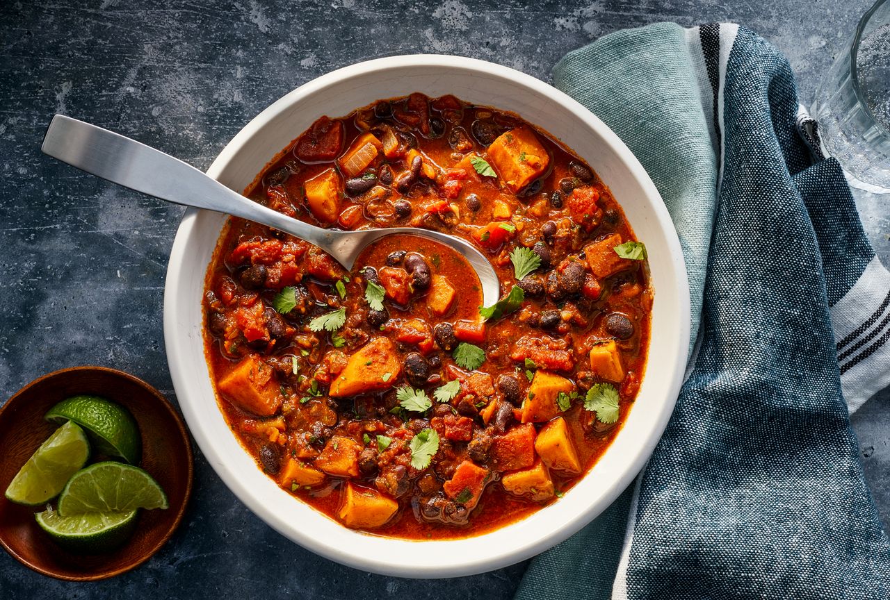 Sweet potato & black bean chili in a white bowl with a spoon in it. Lime wedges on the side and fresh cilantro sprinkled on top Credit: Photographer: Antonis Achilleos, Food Stylist: Emily Nabors Hall, Prop Stylist: Kay Clarke
