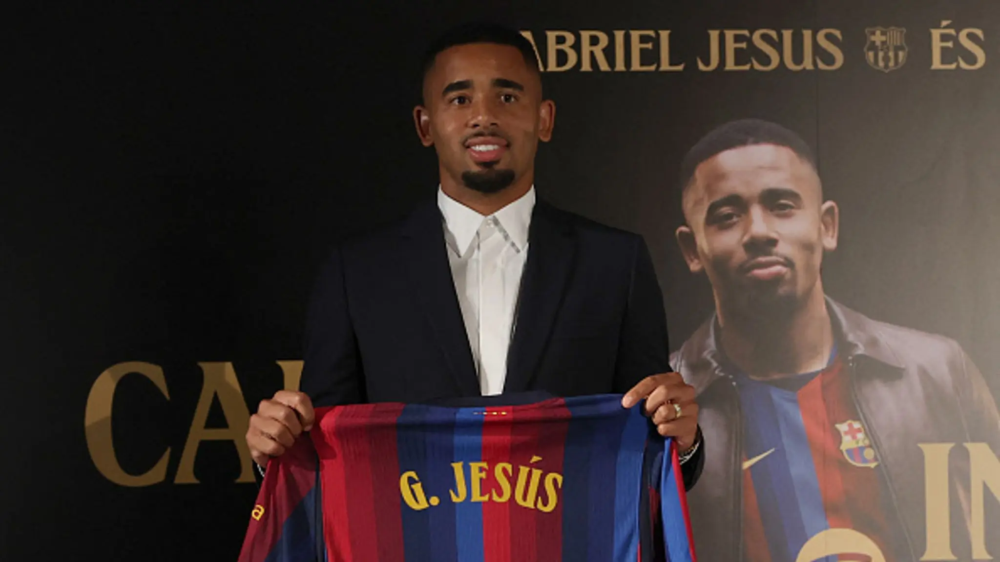 Gabriel Jesus in a suit holding a FC Barcelona jersey with his name on the back