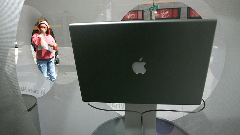 A woman looking through a window at an older Apple MacBook, showing a metallic apple logo
