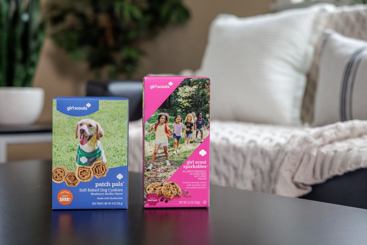 Girl Scout cookie boxes on a table one featuring a dog and the other a group of girls outdoors Credit: Courtesy of Girl Scouts of the USA.