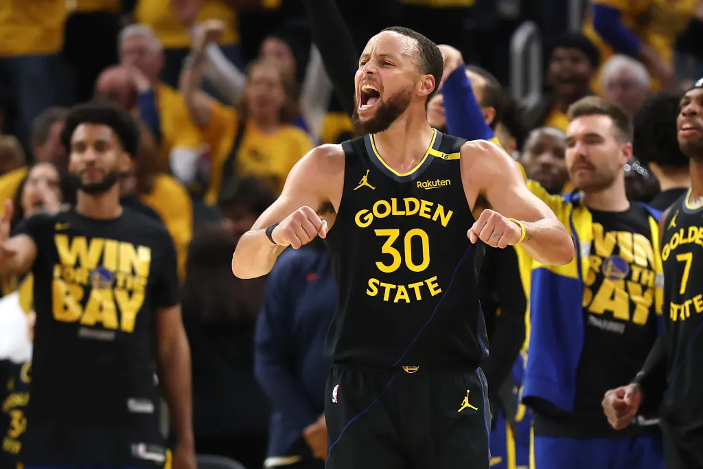 Stephen Curry in a black and gold Golden State Warriors jersey yelling with clenched fists.