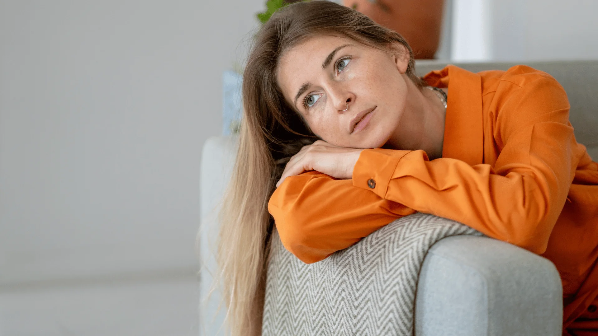 woman in orange shirt thinking i don't have the energy for much as she lays on couch