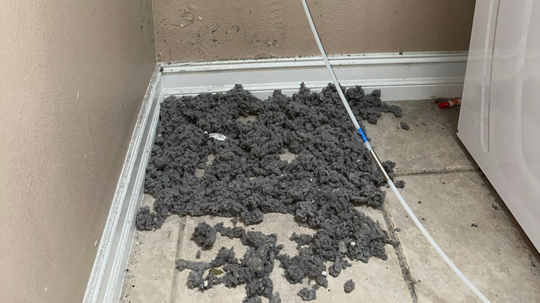 A pile of dryer lint beside a washing machine.