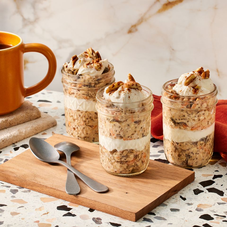 three small jars of carrot cake overnight oats, two spoons, a cloth napkin and a cup of coffee Credit: Photographer: Robby Lozano, Food Stylist: Catherine Jessee, Prop Stylist: Josh Hoggle
