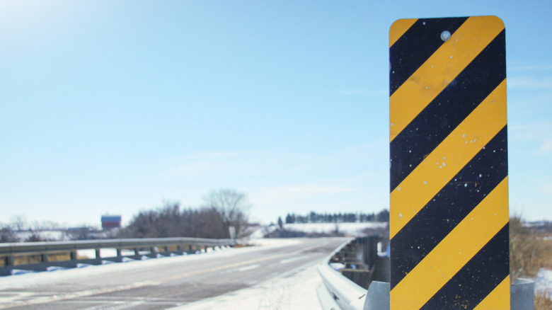 Close up view of black and yellow highway hazard sign placed in front of bridge.