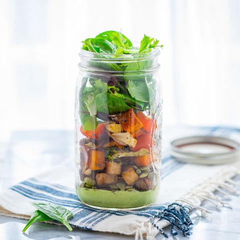 A jar filled with layered salad including greens roasted vegetables and seeds placed on a table with a napkin Credit: EatingWell