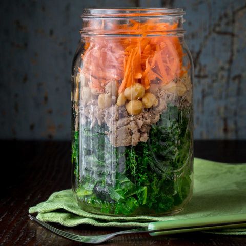 Layered salad in a jar featuring greens chickpeas tuna and shredded carrots placed on a green napkin with a fork nearby Credit: EatingWell