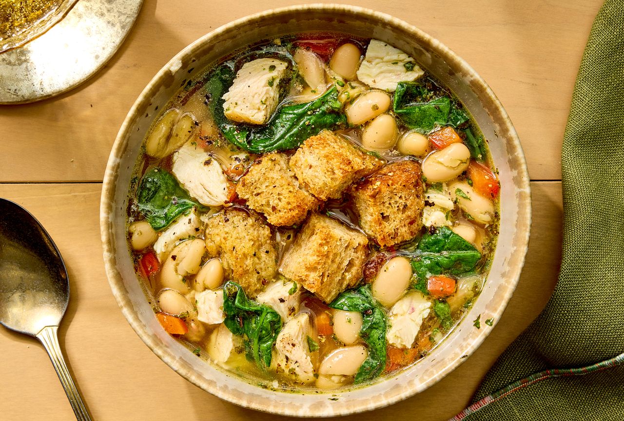 Bowl of chicken and spinach soup with croutons and white beans placed on a wooden table Credit: Photographer: Robby Lozano, Food Stylist: Jennifer Wendorf, Prop Styling: Abby Armstrong