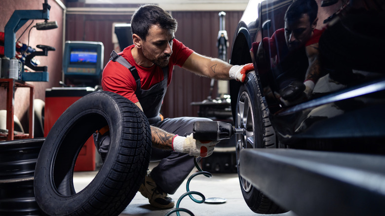 Professional removing the tire from a car with the replacement tire kept on the side