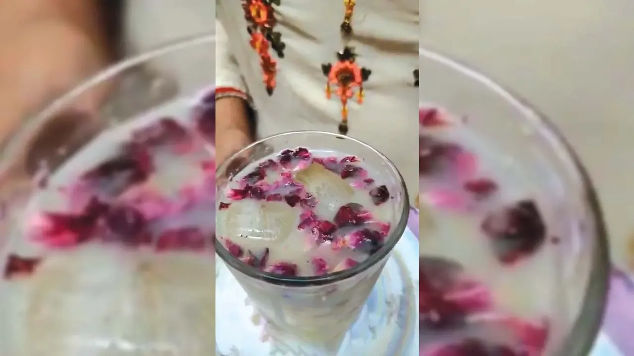 Chilled rose petal milk drink with floating ice cubes served in glass by person wearing traditional embroidered kurta.