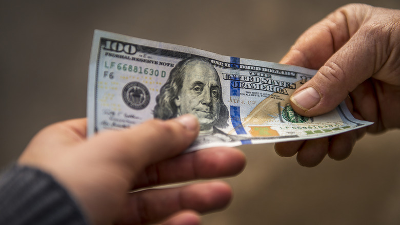 A close-up shot of a person passing a $100 bill to another person.