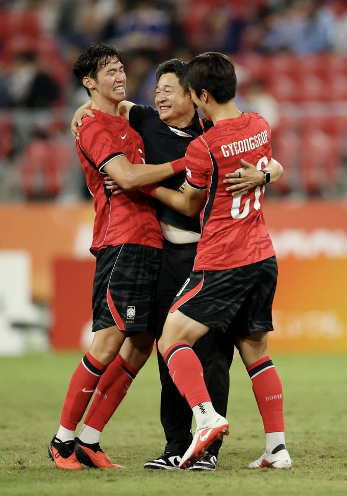 Captain Lee Gi-hyuk (L) celebrates with coach Lee Min-sung and Park Kyung-seop (R) after winning the 2026 Asian Games mens football gold medal. Photo by Reuters.