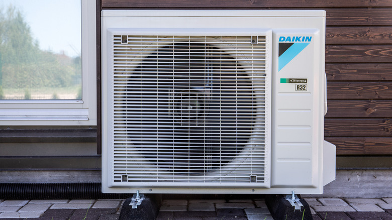 outdoor Daikin air conditioner unit up against a wooden plank wall with a window