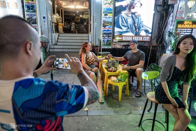 A local helps two foreign visitors capture a moment in Hanoi. Photo by Read/Giang Huy