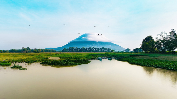 Ba Den Mountain rises above the green plains of Tay Ninh, with clouds gathering around its summit. Photo by Truong Anh Tuan